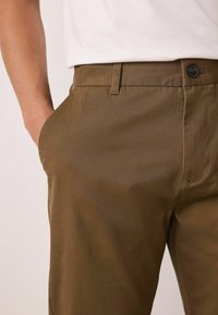 Pruunid, tekstuuriga sirge lõikega püksid. Omavad küljetaskuid ja nööbiga sulgemist, sileda viimistluse ja neutraalse värviga.