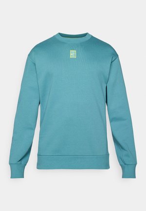 Turkos sweatshirt med ribbad tydelse, rundad hals och långa ärmar. Har en liten gul logotyp i ett rektangulärt mönster på bröstet.