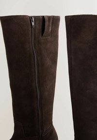 Bruine suède laarzen tot de knie met een zijrits, minimale stikdetails en een soepele textuur.