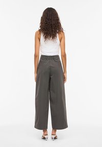 Leveälahkeiset, korkeavyötäröiset housut tummanharmaasta puuvillakankaasta, joissa on joustava vyötärönauha ja takataskut, yhdistetty valkoiseen hihattomaan toppiin.