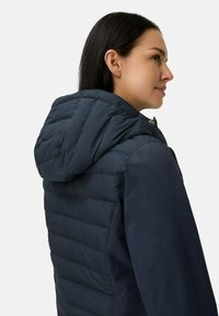 Marineblauwe gewatteerde jas met capuchon, met een doorgestikt ontwerp, een gladde stoftextuur en een ritsluiting aan de voorkant. Accentueert met een platte kraag.