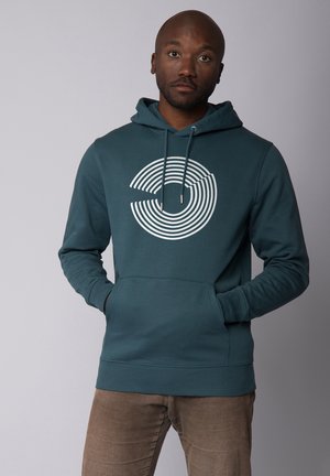 Tegenvloeiende hoodie in teal met een witte geconcentreerde cirkelsgrafiek, verstelbare trekkoordkap en een voorzak; zachte textuur en aansluitende manchetten.