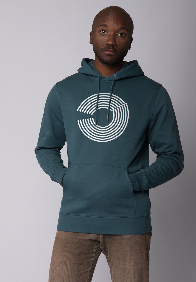 Tegenvloeiende hoodie in teal met een witte geconcentreerde cirkelsgrafiek, verstelbare trekkoordkap en een voorzak; zachte textuur en aansluitende manchetten.