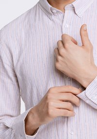 Camicia chiara con bottoni, decorata da sottili righe blu, con colletto a pieghe e polsini con bottoni. Mani che sistemano la camicia al colletto.