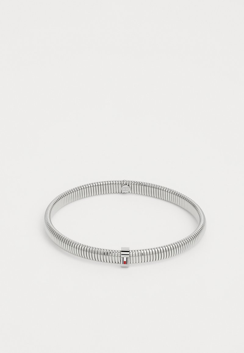 Bracciale in metallo di colore argento, a spirale, con un piccolo fermo rettangolare che presenta un dettaglio rosso e nero, esposto su uno sfondo bianco.