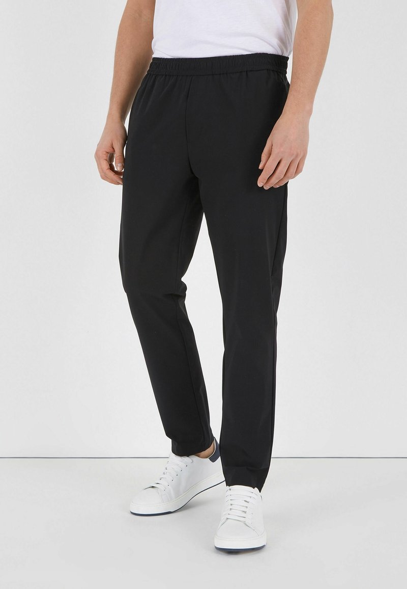 Sorte atletiske bukser med elastisk talje, tapered ben design og glat tekstur, parret med hvide sneakers.