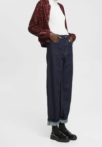 Bordeaux sequin bomberjakke over en hvid turtleneck, parret med mørk denim højtaljede bukser opsmøgede ved stropperne og sorte sko.