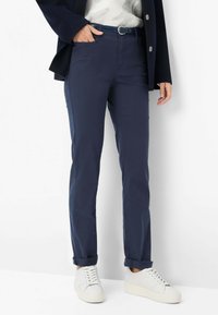 Pantaloni blu navy slim fit, con cintura con fibbia argentata, orli risvoltati e abbinati a sneaker bianche. Tessuto dalla texture liscia.