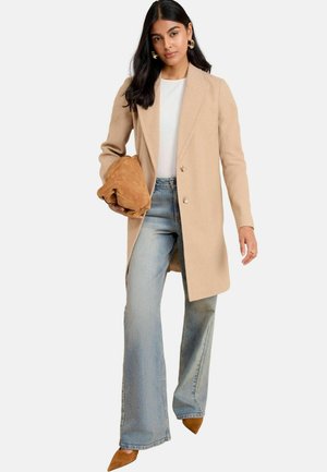 Beige wollen blend jas met een getailleerd ontwerp, twee knopen en een geknipt kraag, gecombineerd met lichtblauwe flared jeans en bruine suède hakken.