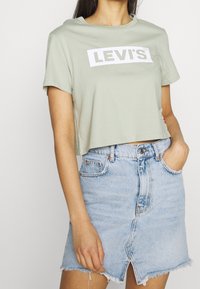 Ljusgrön kortärmad t-shirt med en vit "LEVI'S"-logotyp. Matchad med en ljusblå denimkjol med fransad nederkant och framfåra.