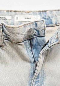 Jeanși din denim albastru deschis, cu închidere cu nasture metalic, cusături contrastante și fermoar. Materialul are o textură ușor decolorată.