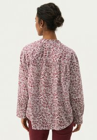 Long-sleeve shirt featuring a white fabric with small red floral patterns, gathered detailing at the back, and buttoned cuffs.