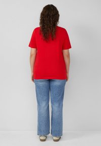 Rotes Baumwoll-T-Shirt mit kurzen Ärmeln, kombiniert mit hellblauen Schlagjeans. Das Outfit zeichnet sich durch eine lockere Passform und ein einfaches Design aus.