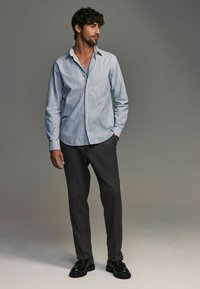 Camisa de botones a rayas azul claro y blanca, pantalones grises, zapatos negros. Tela suave, diseño ajustado, mangas largas y collar abierto.