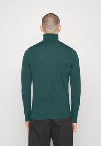 Teal Strick-Turtleneck-Pullover mit langen Ärmeln. Figurbetontes Design mit geripptem Muster am Kragen und den Säumen. Weicher Stofffinish.