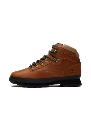 Brauner Leder-Timberland-Wanderschuh mit schwarzer Sohle, gepolstertem Knöchelkragen, Metallösen und schwarzen Schnürsenkeln, seitlich dargestellt.