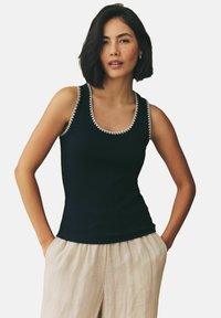 Sort tanktop med ribbet tekstur, udsmykket halsudskæring med hvid detaljering, parret med lyse linnedbukser.