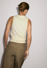 Top senza maniche di un giallo chiaro con un design aderente, abbinato a pantaloni larghi in lino marrone con tasche posteriori. Struttura del tessuto naturale visibile.