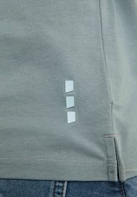 Graues Baumwoll-T-Shirt mit drei eingebetteten rechteckigen Etiketten in Hellblau auf der linken Seite, mit sichtbarer Saumnaht am unteren Rand.