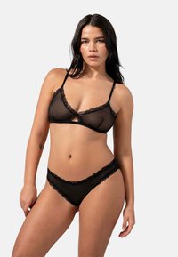 Set di lingerie nera trasparente con bralette decorato in pizzo e spalline regolabili, abbinato a slip accentuati in pizzo.