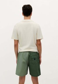 Heren polo met korte mouwen in lichtbeige met een gladde textuur, gecombineerd met olijfgroene shorts met een elastische tailleband en een patchzak.
