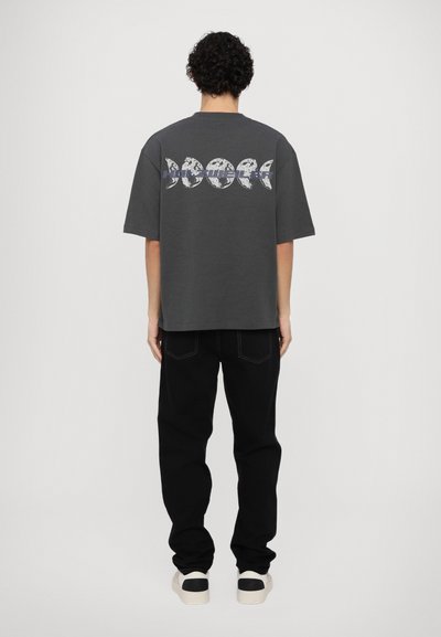 T-shirt gris à manches courtes avec un graphique des phases de la lune au dos, associé à un jean noir et des baskets claires.