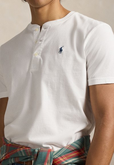 Λευκό βαμβακερό T-shirt με λαιμόκοψη henley, που διαθέτει τρεις κουμπότρυπες και ένα μπλε κεντητό λογότυπο στο αριστερό στήθος.