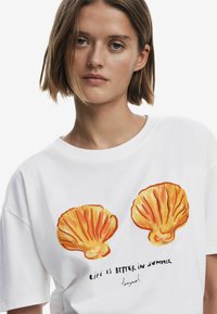 Hvid T-shirt med to orange skaldillustrationer og teksten "LIVET ER BEDRE OM SOMMEREN." Korte ærmer, blødt bomuldsstof.