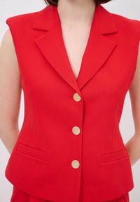 Rotes ärmelloses Blazer mit Reverskragen, ausgestattet mit goldfarbigen Knöpfen und zwei Vordertaschen. Glattes Material und taillierte Passform.