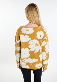Maglione a maglia giallo senape, con un ampio motivo floreale bianco. Vestibilità morbida, scollatura ampia e maniche lunghe. Morbido al tatto.
