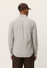 Ριγέ βαμβακερό πουκάμισο με γιακά, μανσέτες με κουμπιά και καμπυλωτό τελείωμα. Η παλέτα χρωμάτων περιλαμβάνει ανοιχτό γκρι και λευκές ρίγες.