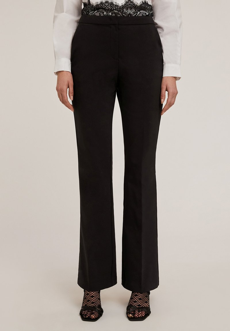 Svarta skräddarsydda byxor med rak benform, slät matt textur och framfickor, ihop med nätstrumpor.