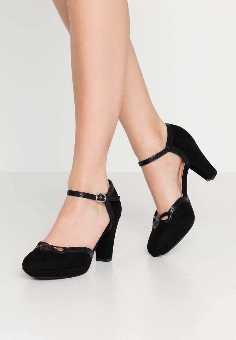 Chaussures à talons hauts en daim noir avec un bout arrondi, une sangle de cheville réglable et un design découpé décoratif à l'avant.