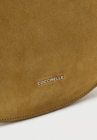 Brown suede handbag with a smooth texture, featuring a silver "Coccinelle" logo and rounded shape with clean stitching edges.
