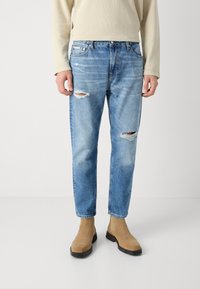 Ljust blå slitna jeans med hål, klassisk femfickdesign, rak benstil, sliten textur, kombinerade med beige chealseastövlar.