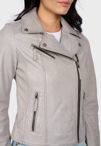 Giubbotto da motociclista in pelle grigio chiaro con colletto a scollo, zip asimmetrica e diverse tasche con zip. Texture liscia con dettagli di cucitura.