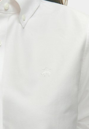 Biała koszula z guzikiem, wykonana z gładkiego materiału, z dyskretnym haftowanym logo na piersi i klasycznym wzornictwem kołnierzyka.