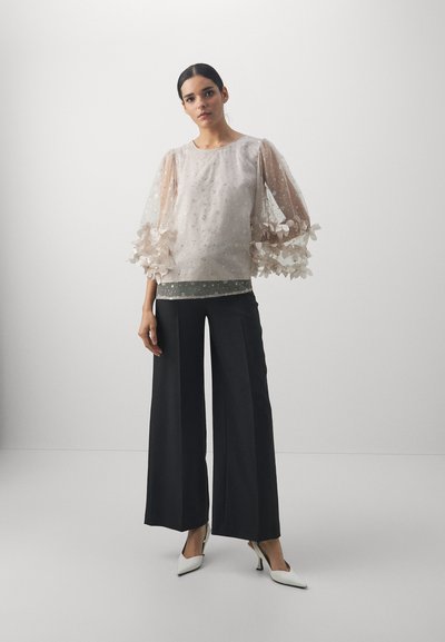 Sheer light pink top with floral embellishments and puff sleeves, paired with wide-leg black trousers and white pointed heels.