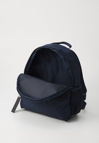 Navy stoff ryggsekk har en rund form, glidelåslukking, stort hovedrom og frontlomme med et strukturert stoffpanel.