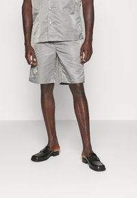 Grå lättvikts kortärmad skjorta med knappar och matchande shorts i ett slätt, glänsande tyg, parat med svarta loafers.