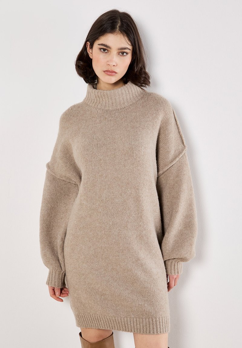 Beiges gestricktes Sweaterkleid mit hohem, geripptem Kragen, überschnittenen Schultern und langen Ärmeln; hat eine lockere Passform und einen gerippten Saum.