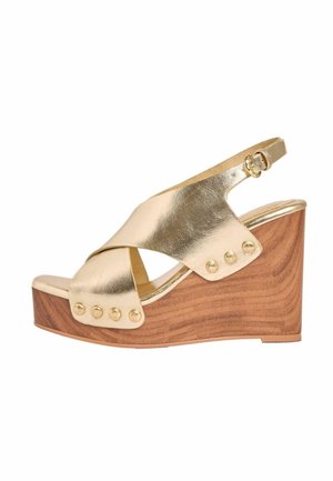 Zlaté kovové wedges sandály s dřevěným podpatkem, s křížovými popruhy a dekorativními nýty. Nastavitelný kotníkový pásek pro bezpečné uchycení.