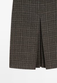Spódnica w kratę z wełny w ciemnym brązie, szarości i czerni. Prosty krój z detalem w postaci rozporka z przodu. Miękka faktura i klasyczny wzór w kratę.