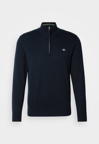 Navy knit pullover with a half-zip neck, ribbed cuffs, and a small embroidered logo on the chest. Smooth texture, casual fit.