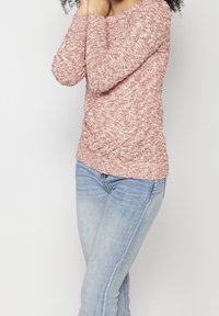 Pull rouge et crème en maille avec manches longues et col rond, associé à un jean bleu clair. Présente un motif texturé et un léger froncé.