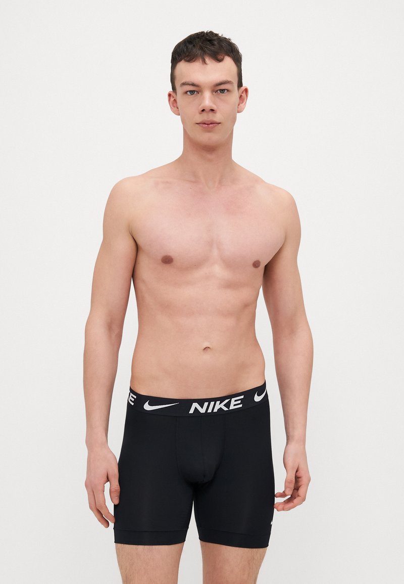 Czarne bokserki stretch z gładkiego materiału z białym logo Nike na pasie. Posiadają dopasowany krój i długość do połowy uda.