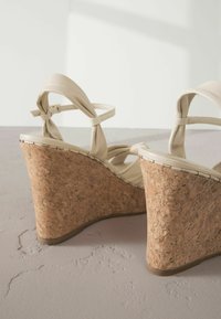 Sandali wedge beige con piattaforma in sughero, dettaglio in sughero testurizzato e cinturini annodati. Materiale superiore liscio con design elegante.