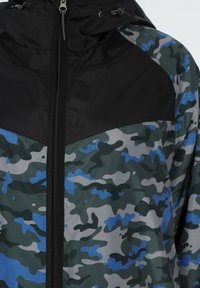 Giacca a vento con un motivo mimetico in tonalità di verde, blu e grigio, con una sezione superiore nera e chiusura con zip.