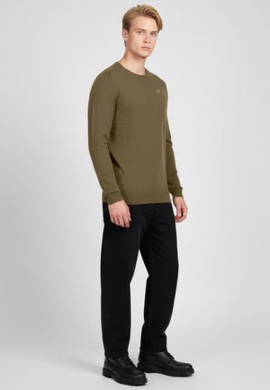 Olijfgroene longsleeve met ronde hals, slim fit en textuurstof; gecombineerd met zwarte broek en zwarte veterlaarzen.