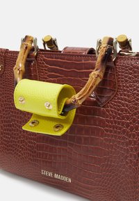 Sac à main marron à motif crocodile avec des poignées en bambou et une sangle amovible verte lime. Quincaillerie dorée et logo en relief sur le devant.